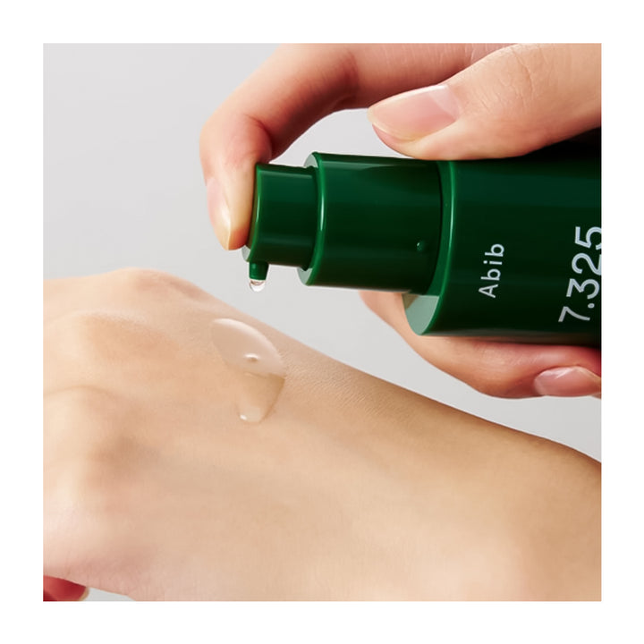 A close-up of a hand dispensing a clear gel-like product from a dark green pump bottle onto another hand. The bottle has white text reading &