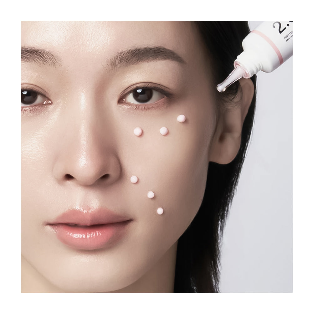 Close-up of a woman's face with small white dots applied to her forehead, cheeks, and chin, while a white skincare dropper tube is being used to apply the product.