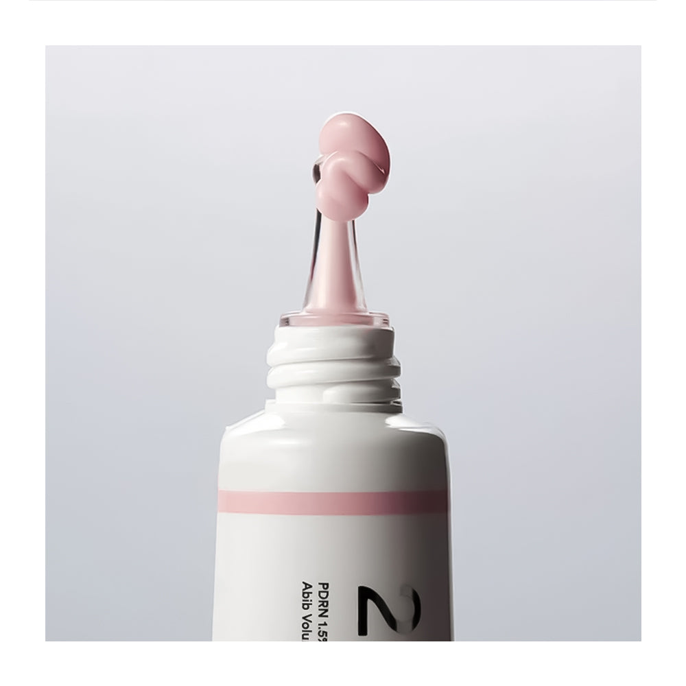 A close-up of a white cosmetic tube with a pink stripe and a dropper-style applicator tip holding a pink product, shown against a light gray background.
