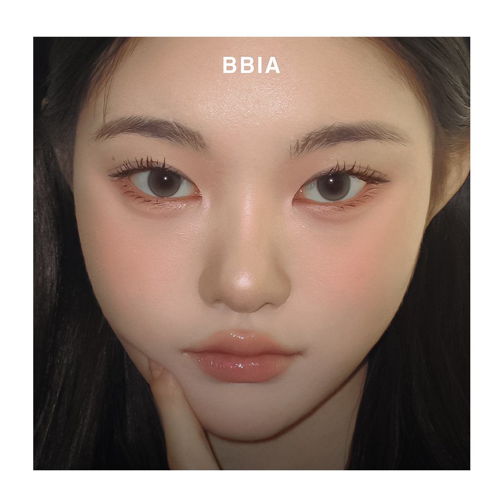 A close-up portrait of a woman with BBIA makeup on her face, showing a glossy nude-pink lip color and warm pink cheek blush. The text 'BBIA' is printed above her forehead.