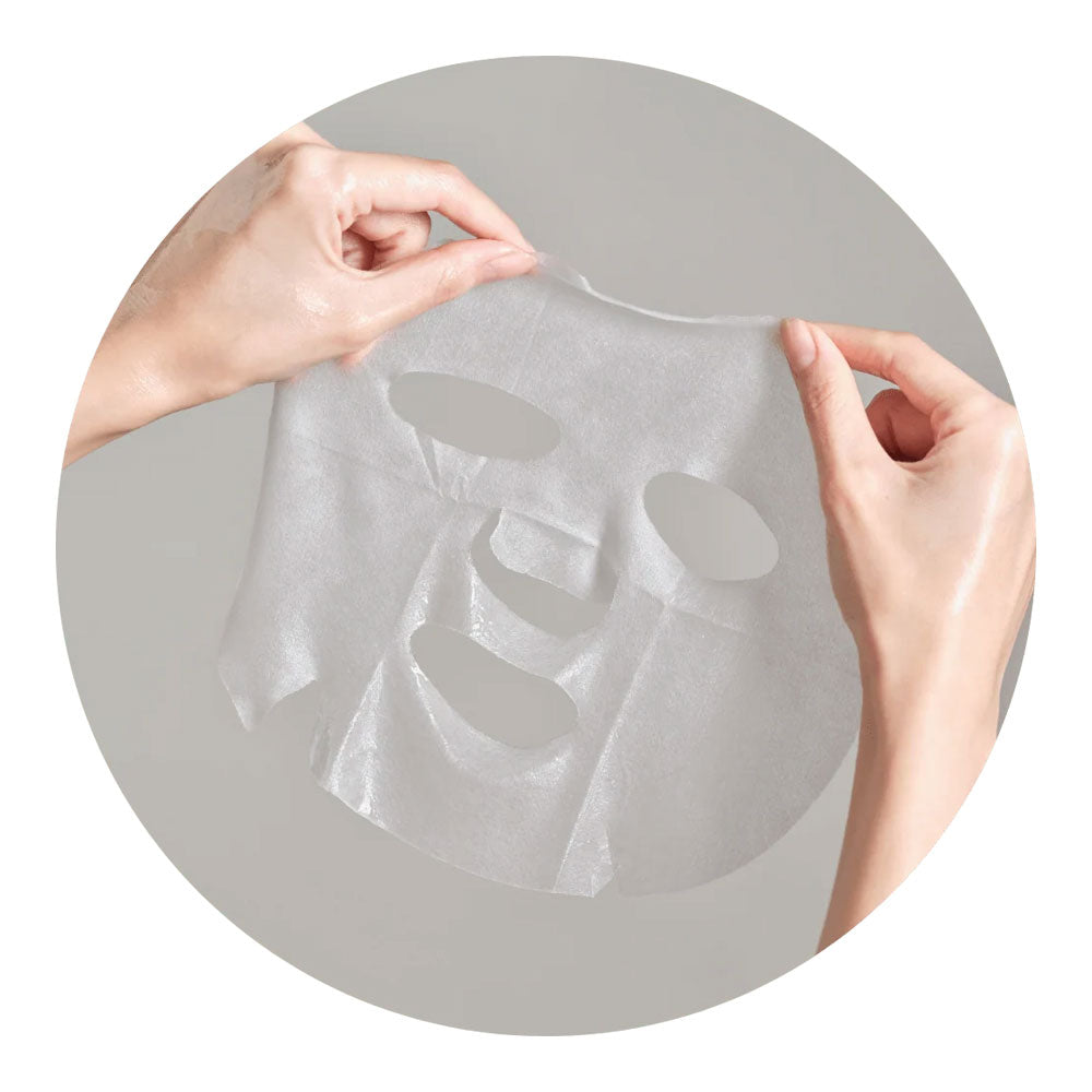 A translucent white sheet mask being held up by two hands against a gray circular background.