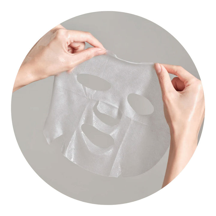 A translucent white sheet mask being held up by two hands against a gray circular background.