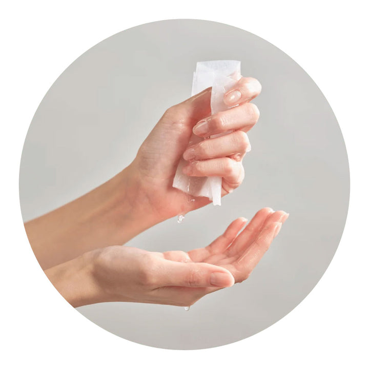 A close-up of hands dispensing a clear gel or liquid from a small translucent packet into an open palm, set against a light gray circular background.