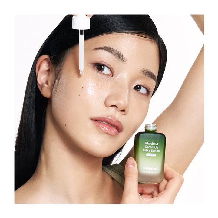 Woman applying a skincare serum to her face with a dropper and holding a bottle of serum.