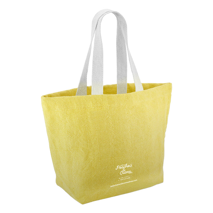 A yellow textured canvas tote bag with white shoulder straps and white script branding on the lower front, shown on a plain white background.