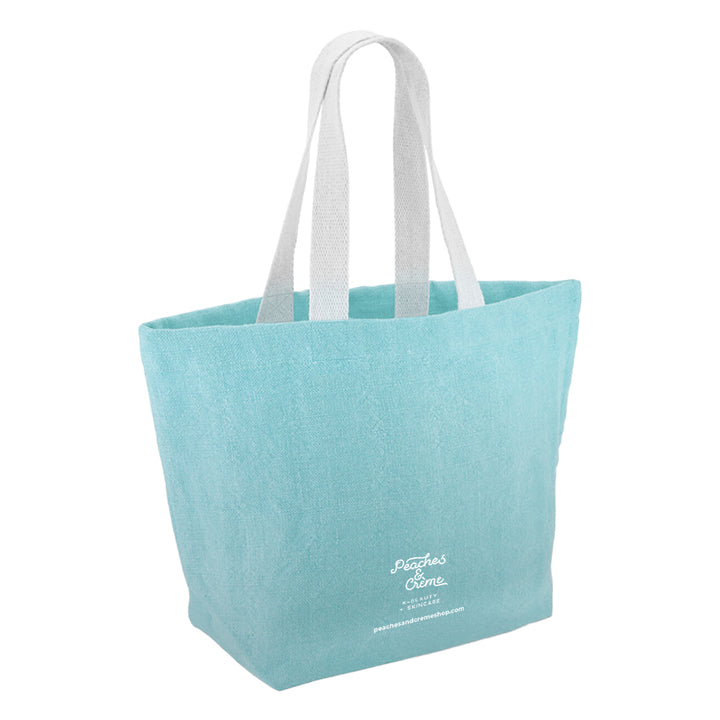 A light blue canvas tote bag with white shoulder straps and white script text on the lower front reading &
