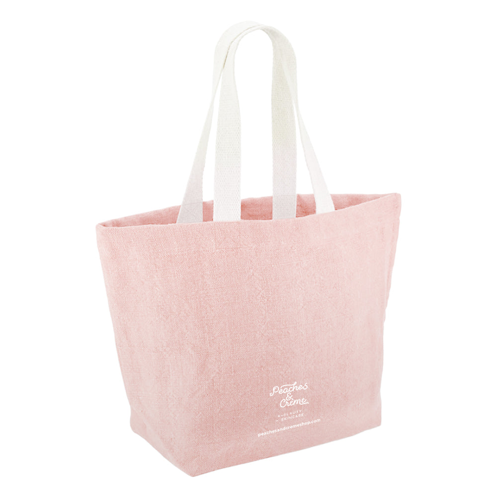A light pink canvas tote bag with white shoulder straps and white printed text near the bottom right, shown on a plain white background.