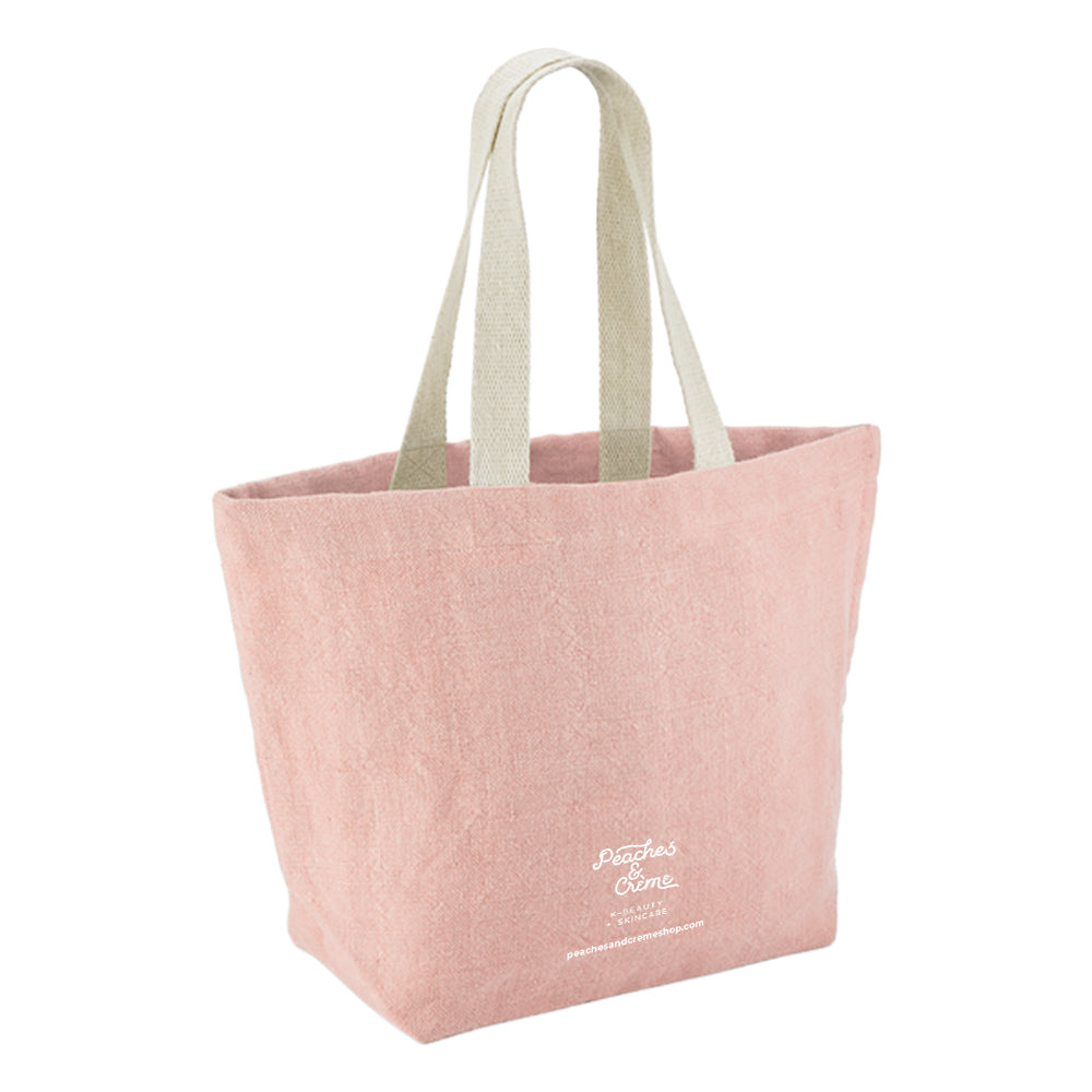 A dusty pink canvas tote bag with light beige fabric shoulder straps and white embroidered &