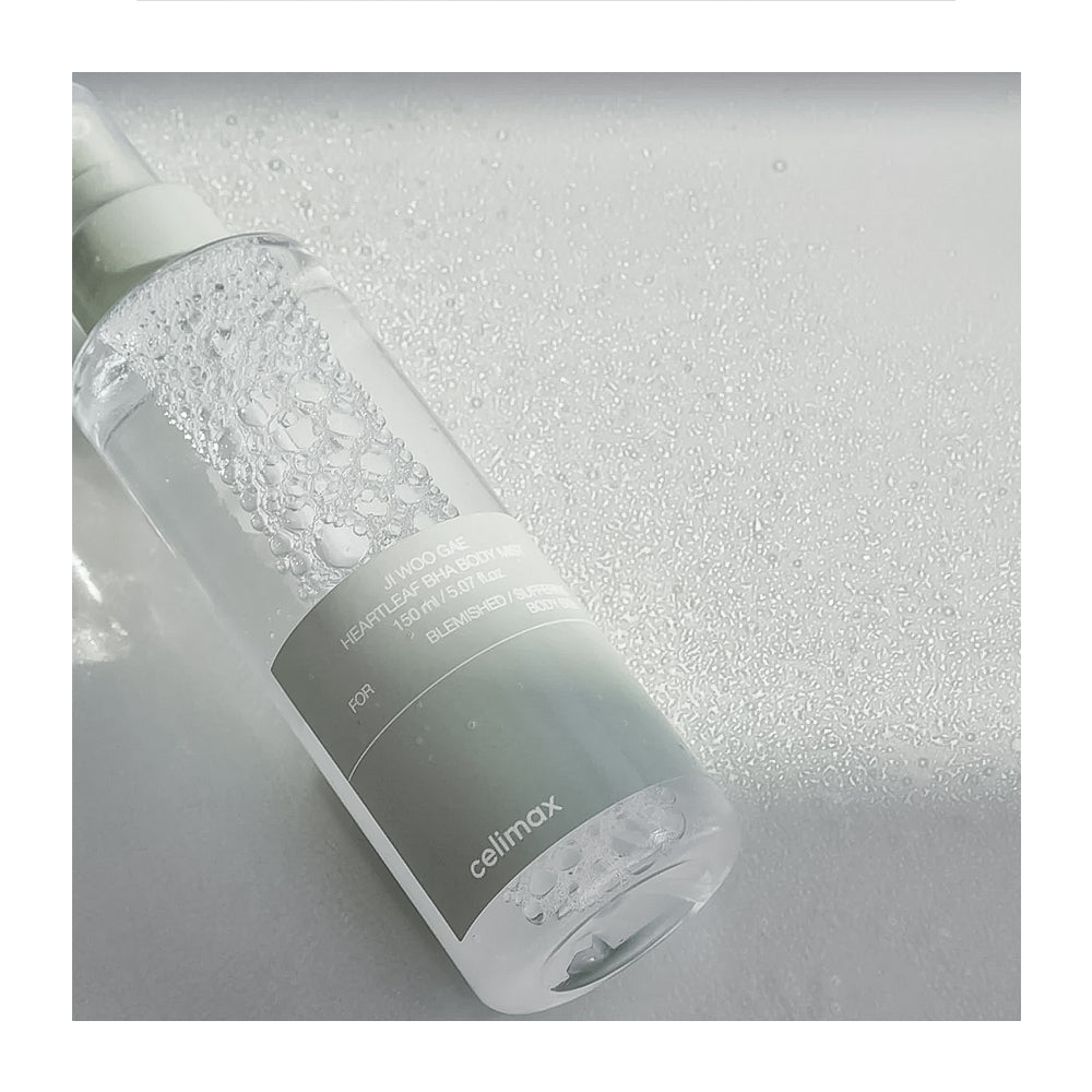A clear cylindrical bottle of Celimax cleansing liquid with a white pump, lying diagonally on a textured light gray surface with water droplets.
