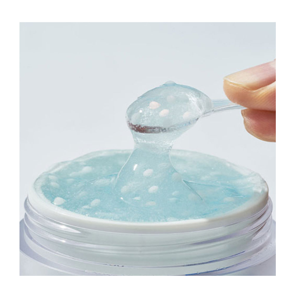 A close-up of a translucent light blue gel or slime-like product being lifted from a clear round container with a white rim, with a hand holding a small spoon at the top right.