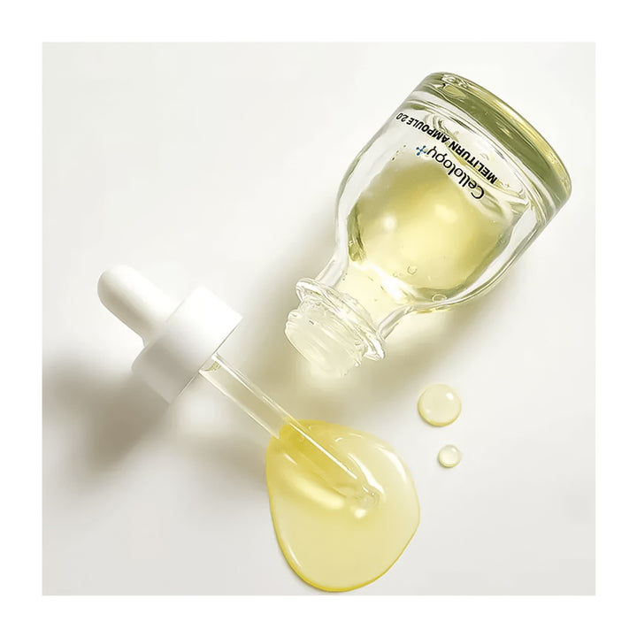 A clear glass dropper bottle containing pale yellow liquid, shown on a white background with the dropper tipped over and the liquid pooling below. The bottle has black text reading &