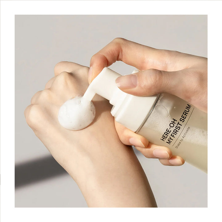 Hand applying serum from a bottle labeled &