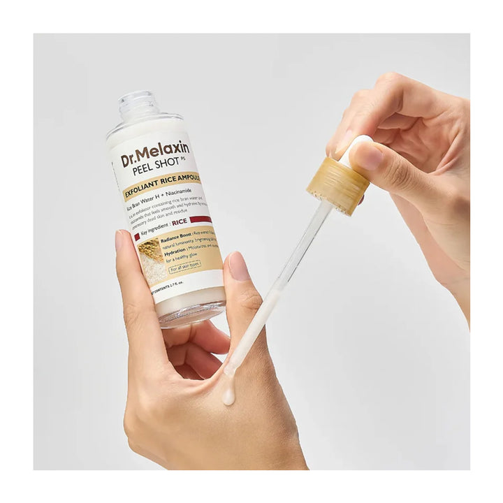 A hand holds a clear bottle of Dr. Melaxin Peel Shot Irriguant Rice Ampoule while another hand dispenses a clear gel dropper onto the back of the hand, against a light gray background.