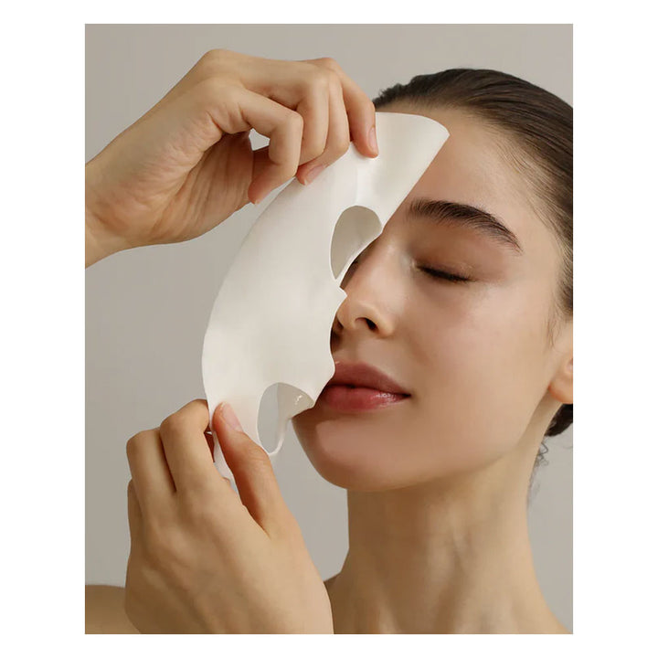 Person applying a white facial mask to their face with a neutral background