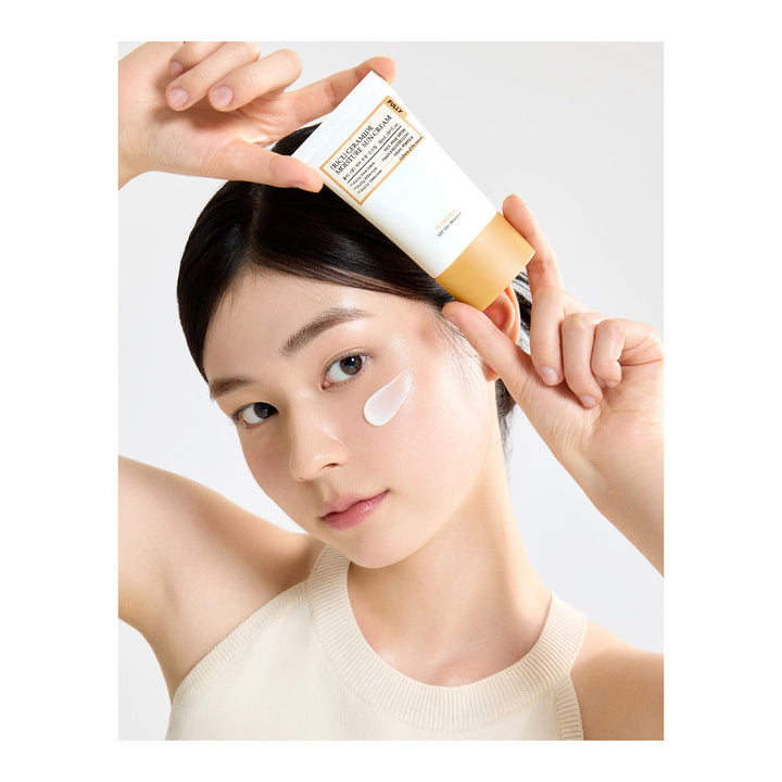 Woman applying cream to her face with a bottle of cream held above her head.