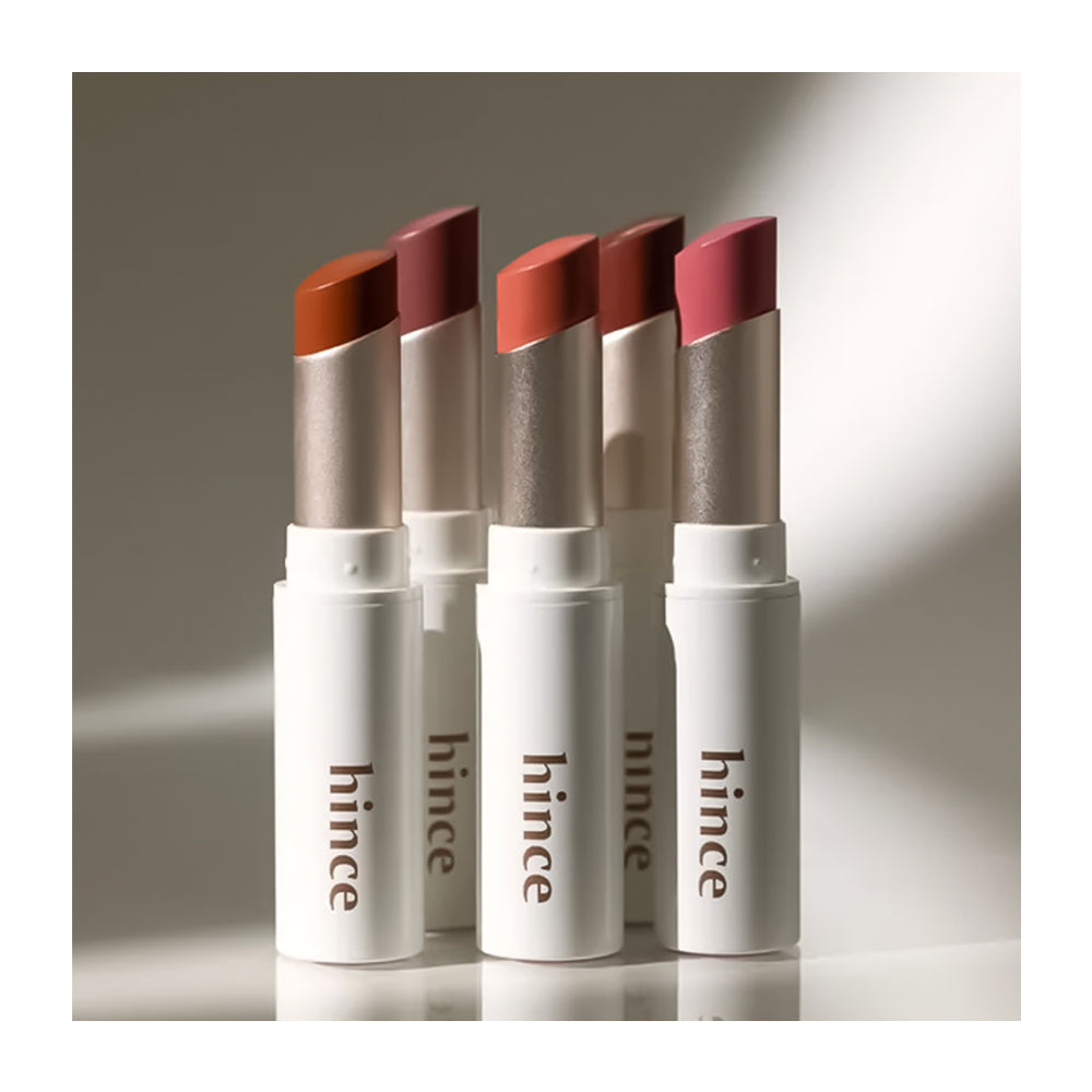 Four lipsticks with different shades in white cases on a neutral background, branded &