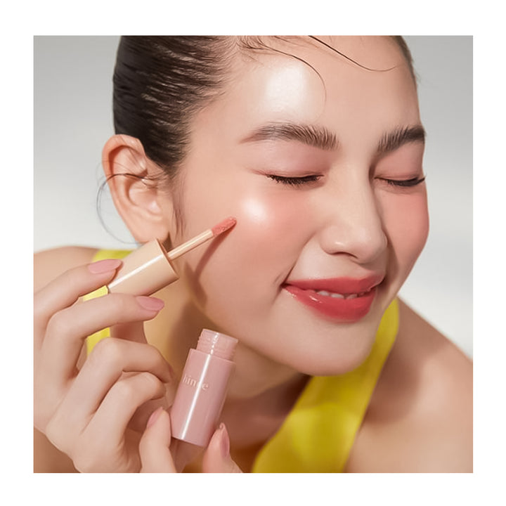 Woman applying makeup with a brush and pink container on a neutral background