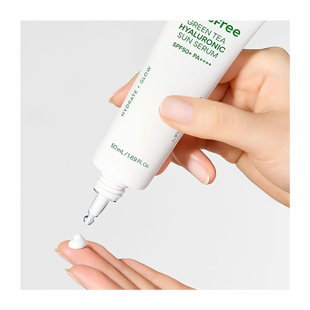 Hand holding a bottle of Green Tea Hyaluronic Sun Serum with a dropper on a light gray background
