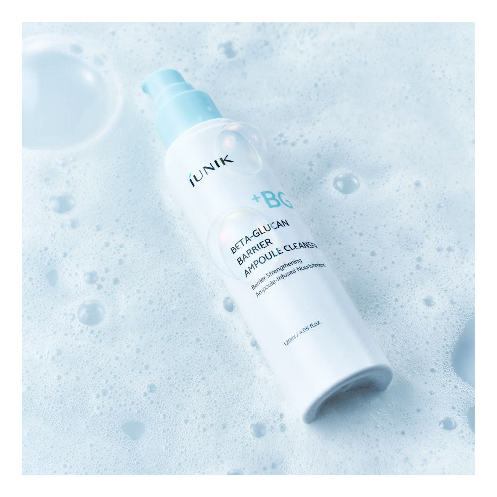 A bottle of iunik Beta-Glucan Barrier Cleansing Amino Acid Cleanser with a light blue pump, resting on a bed of white foam bubbles.