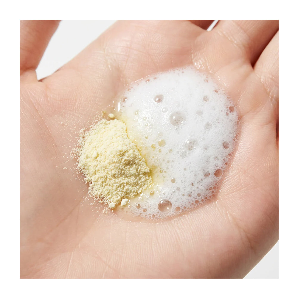 A close-up of a human hand holding a small pile of pale yellow powder next to a pool of white foam.