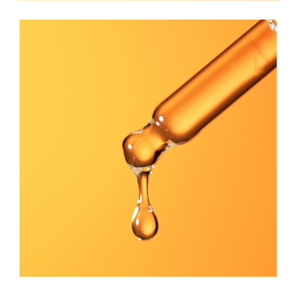 A close-up of a clear glass dropper tube releasing a glossy amber-orange liquid drop against a warm orange background.