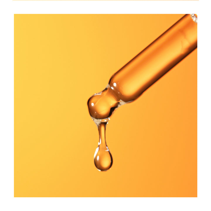 A close-up of a clear glass dropper tube releasing a glossy amber-orange liquid drop against a warm orange background.