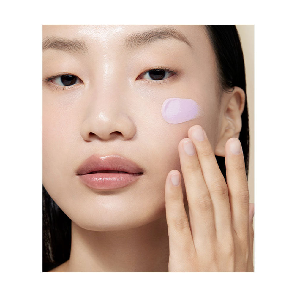 Woman applying a pink cream to her face with a close-up view.