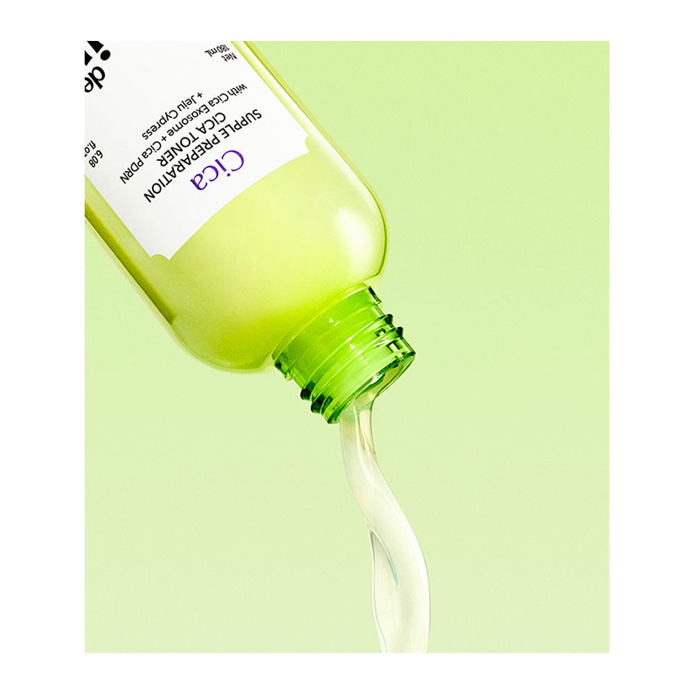 A close-up of a green bottle tilted to pour a pale yellow-green serum, with a curved stream of the liquid dripping out against a light green background. The label shows the brand &