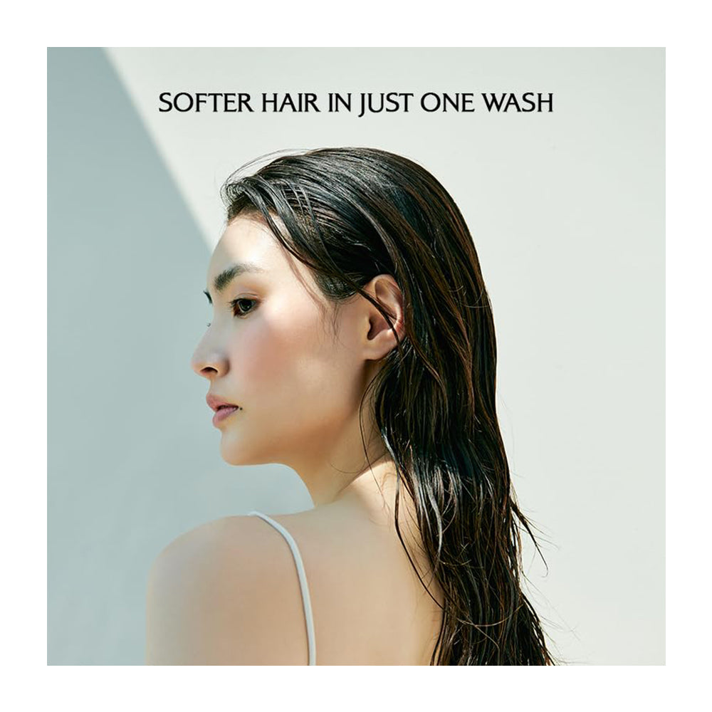 A woman in profile with long, dark, wet hair wearing a white spaghetti-strap top, set against a minimalist light gray background with the text &