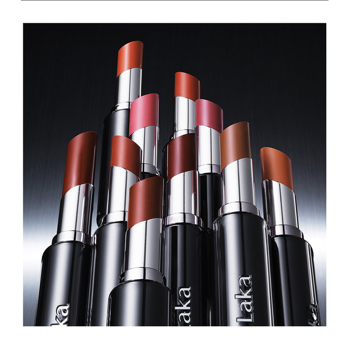 A group of Laka brand lipstick tubes arranged together against a dark gradient background, showing various warm-toned lipstick shades from nude brown to coral and pink.