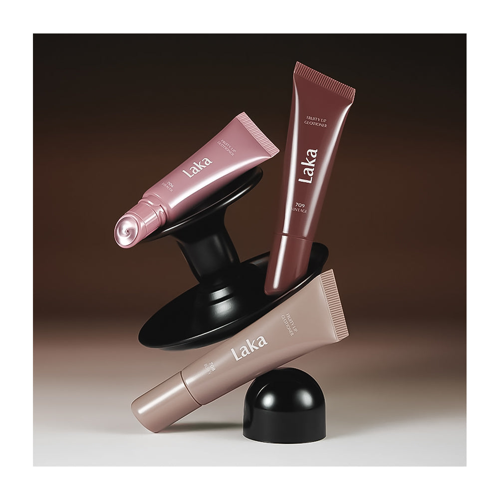 Three Laka cosmetic tubes in pink, mauve, and taupe tones displayed on a black sculptural stand against a dark brown studio background.