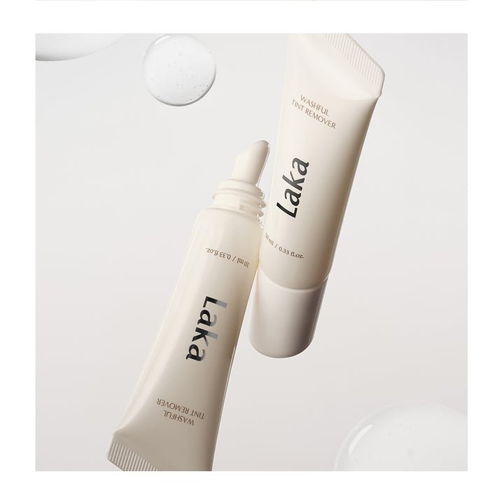 Two white cosmetic tubes of Laka Natural Fine Tini Remover, one standing upright and the other lying diagonally, on a clean white background with soft decorative droplets.