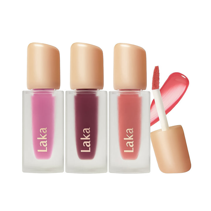 Three Laka liquid lipstick tubes in pink, mauve, and coral shades with beige caps, shown on a white background with one cap removed and the applicator displayed.