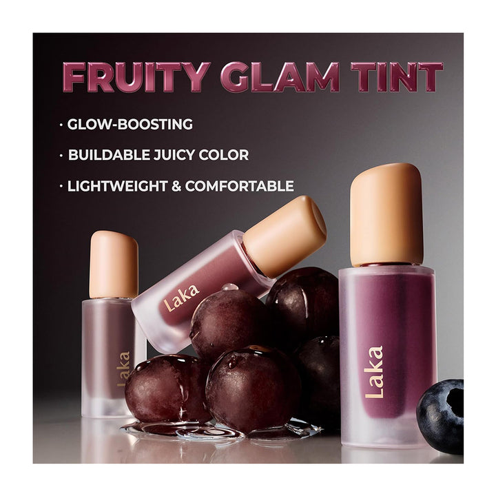 Three bottles of Laka nail polish with a glossy fruit-themed tint, shown with grapes and a blueberry on a reflective surface against a dark gradient background. Text on the image reads &