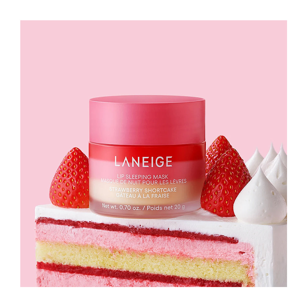 LANEIGE Strawberry Shortcake lip sleeping mask jar styled on a slice of pink and yellow cake with fresh strawberries and white meringue against a solid pink background.