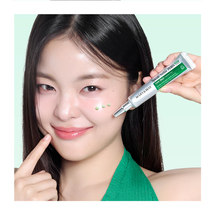 A close-up of a woman with dark hair holding a green and white tube of Mary Mary Skin Care product near her cheek, with a light mint green background.