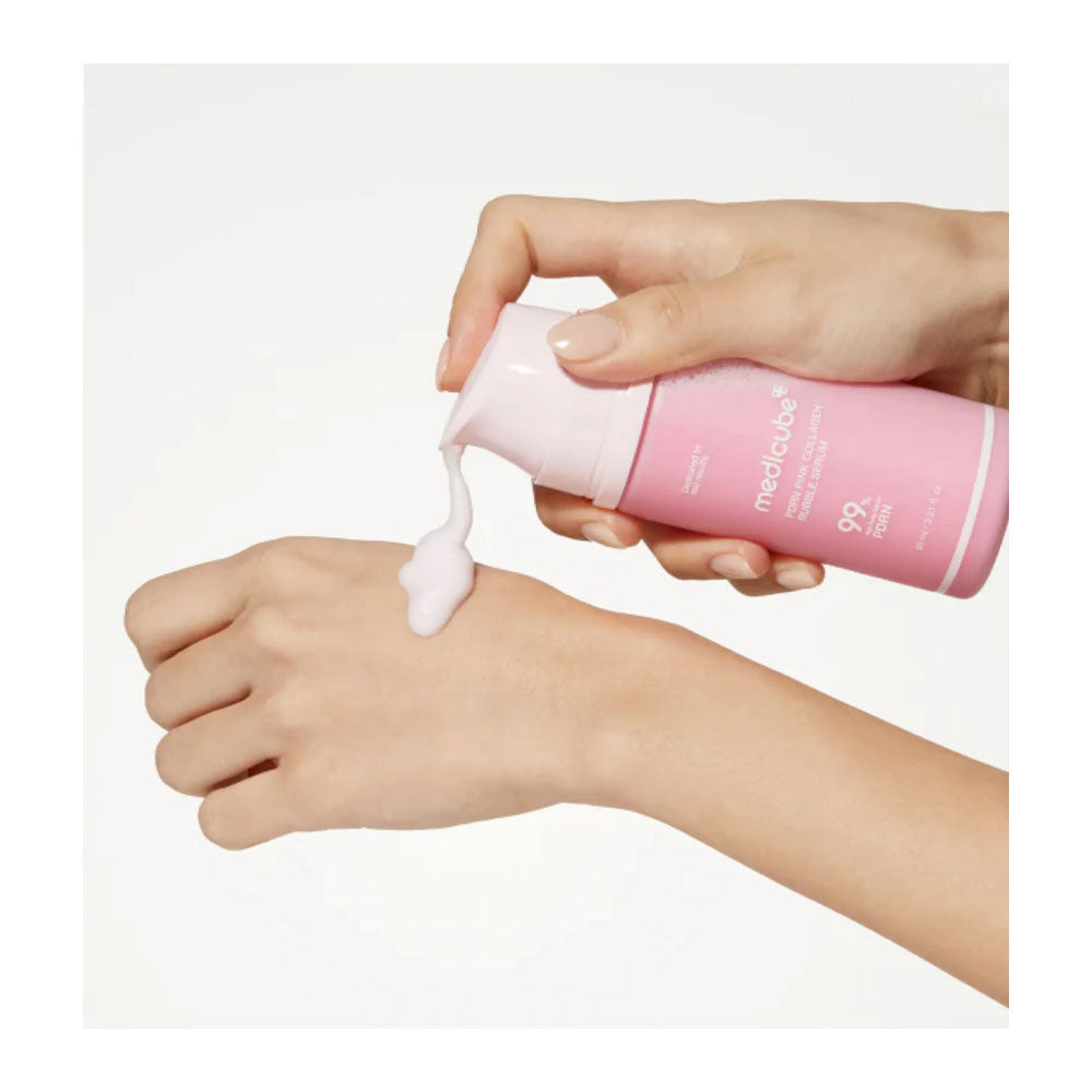 A hand pumps a pink bottle of Medifee Q10 Moisturizing Cream, dispensing a thick white cream onto the back of another hand, set against a clean white background.