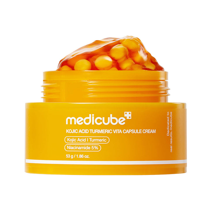 A jar of medicube Kojic Acid Turmeric Vita Capsule Cream, featuring a bright yellow-orange container with a scoop of the orange gel and visible yellow capsules on top, set against a plain white background.
