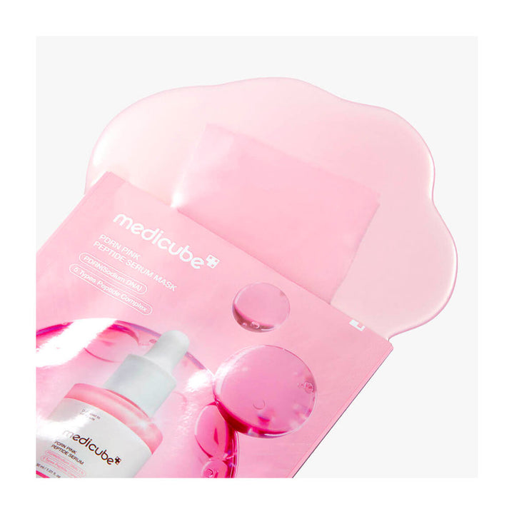 Medicube Global/Local Serum Series facial sheet mask pouch in pink, with a translucent pink sheet partially pulled out and a small dropper bottle shown at the lower left on a light gray background.