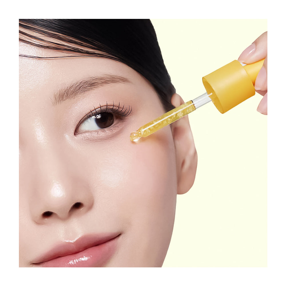 Close-up of a woman applying a yellow dropper to her eye with a clear liquid.