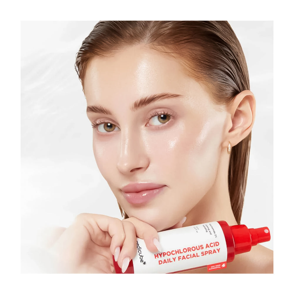 Woman holding a red and white facial spray bottle with a plain background