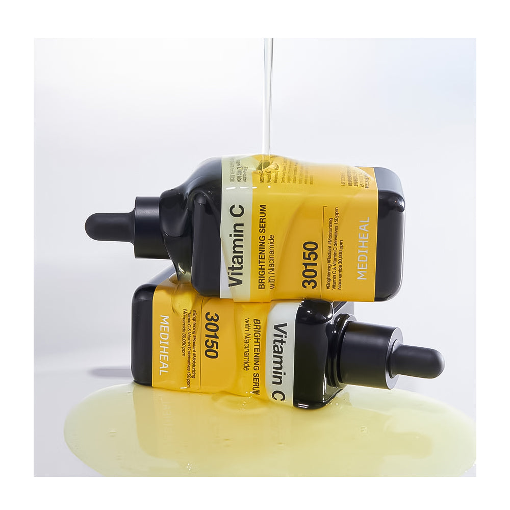 Two MEDHEAL Vitamin C Brightening Serum dropper bottles stacked together on a white surface with a small pool of pale yellow serum below. A clear liquid is being poured into the top bottle against a clean white background.
