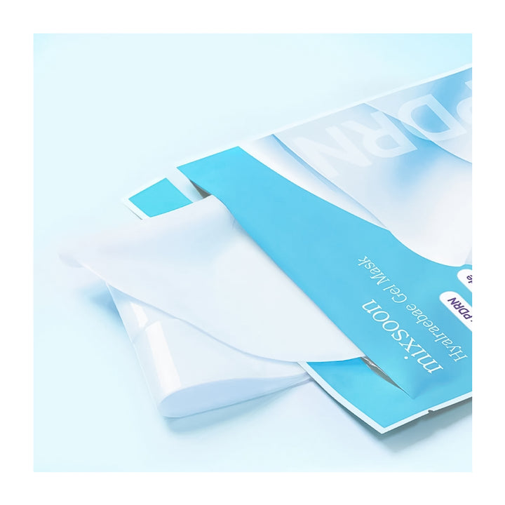 A close-up of a sheet mask package in light blue and white, with a translucent white mask partially peeled back, on a pale blue background.