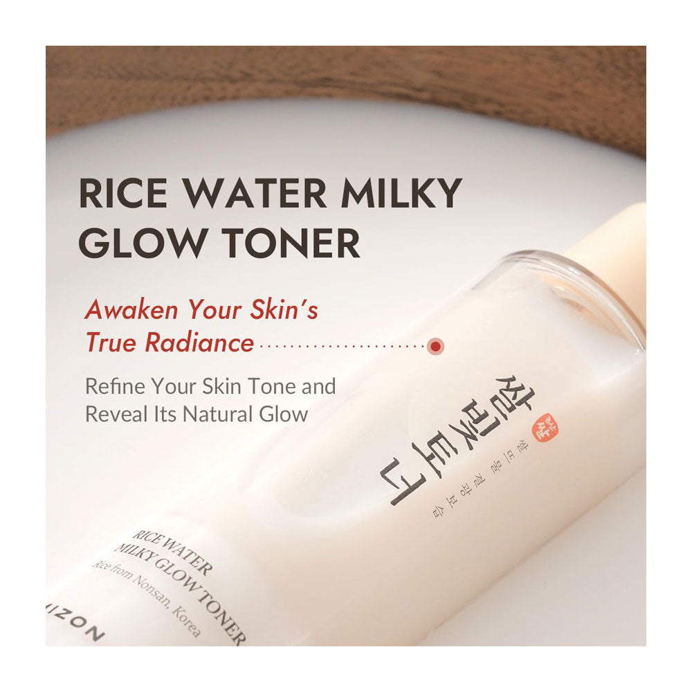 A bottle of Rice Water Milky Glow Toner by Mizon, shown at an angle on a white surface with a brown textured background. The packaging is off-white with black and red text.