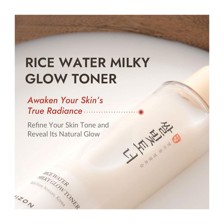 A bottle of Rice Water Milky Glow Toner by Mizon, shown at an angle on a white surface with a brown textured background. The packaging is off-white with black and red text.