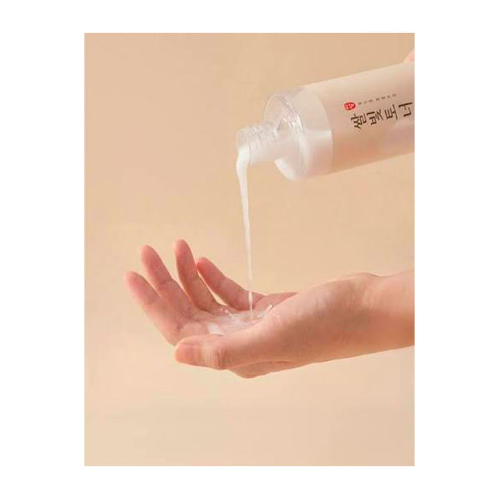 A hand holding open a clear bottle and pouring a translucent white gel or liquid onto the palm, shown against a plain warm beige background.