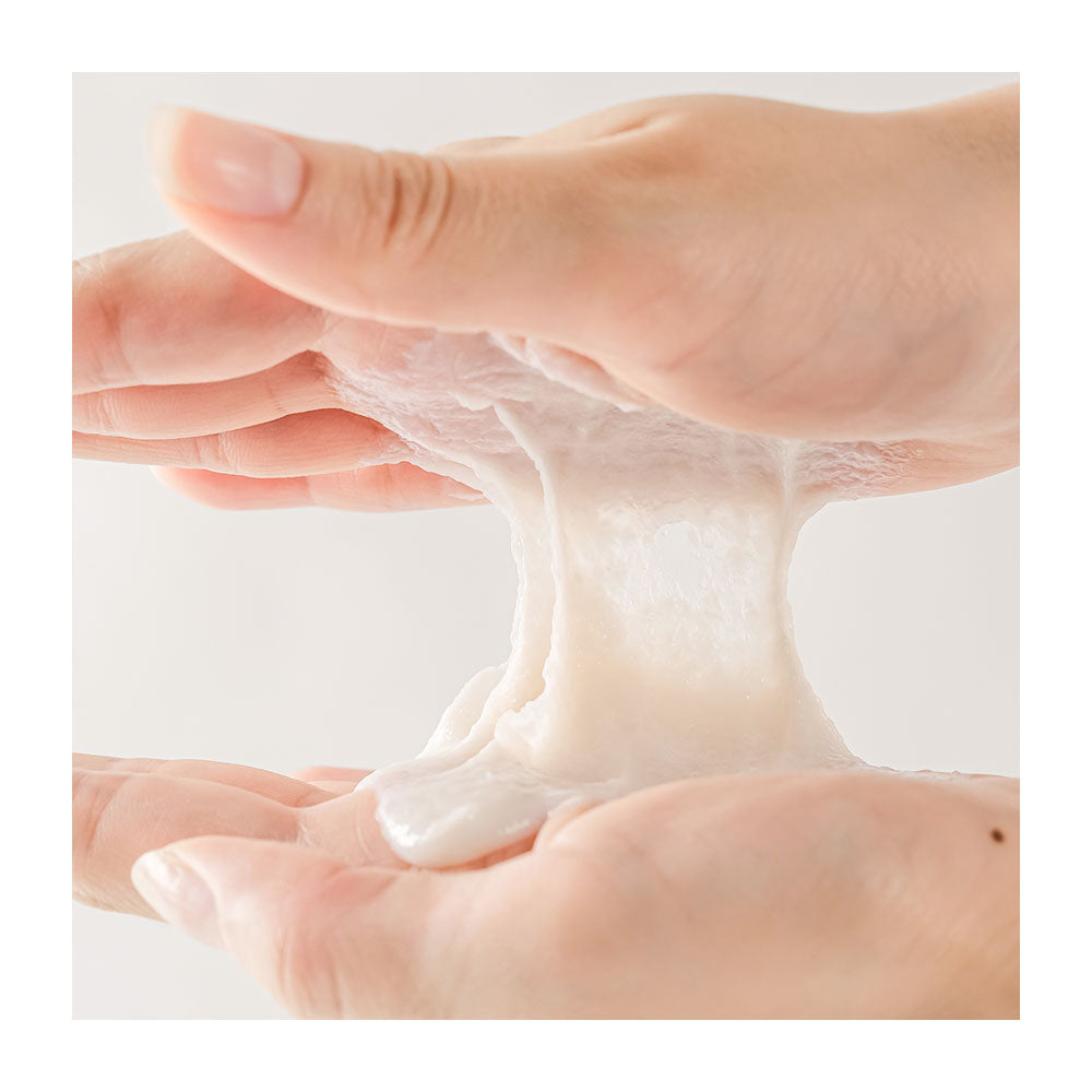 A close-up of two hands stretching a thick, glossy, translucent white cosmetic gel or slime-like substance between the palms against a soft light gray background.