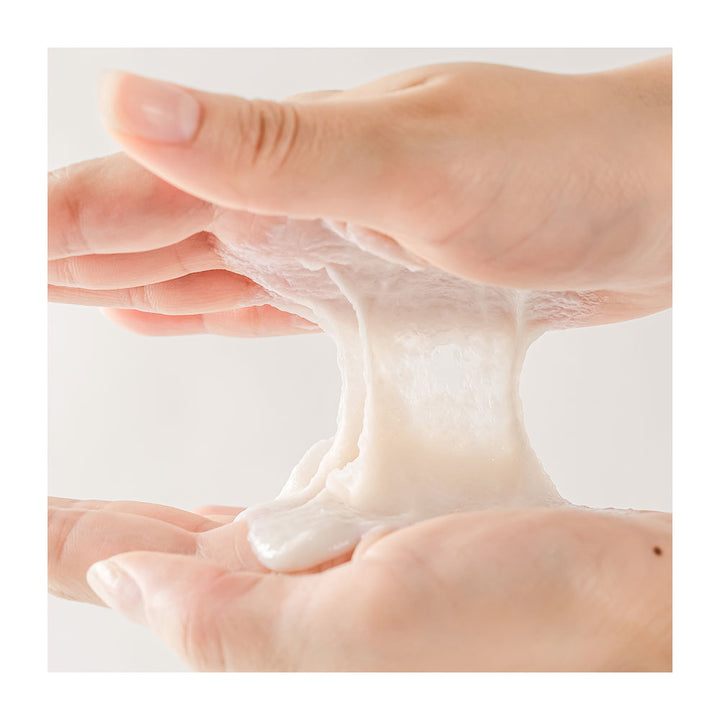 A close-up of two hands stretching a thick, glossy, translucent white cosmetic gel or slime-like substance between the palms against a soft light gray background.