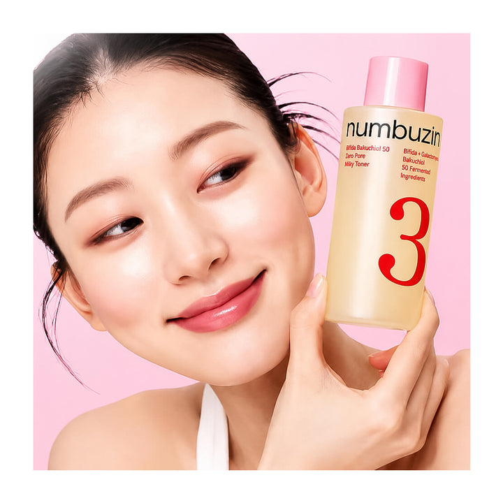 A woman with a radiant complexion holds a bottle of numbuzin Skin Refining Oil No. 3 against a soft pink background.
