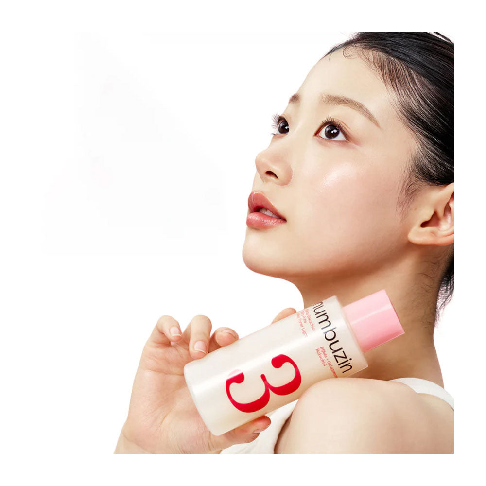 A woman in a white top holds a bottle of skin oil against her shoulder. The bottle is frosted white with a pink cap and features a large red '3' on the front, with the brand name 'skin outzin' visible.